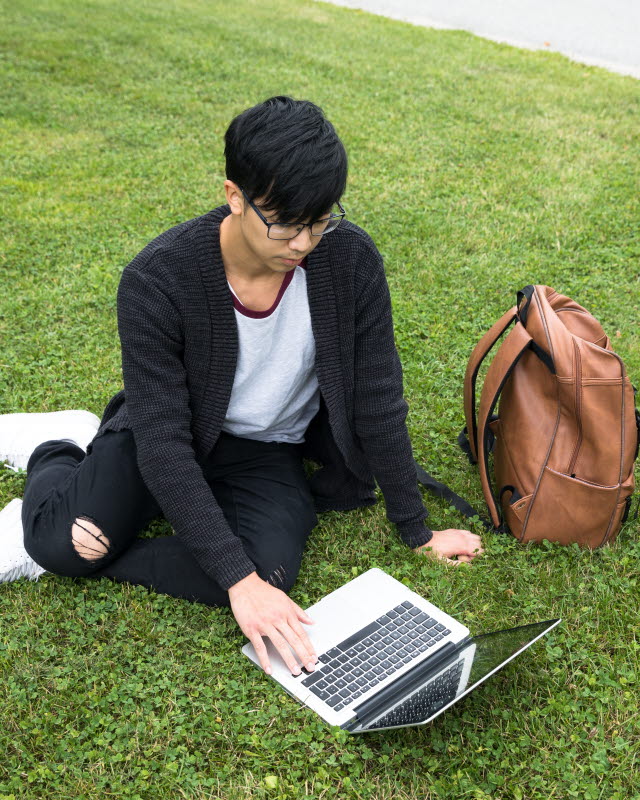 Kille sitter i gräset med sin laptop