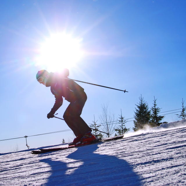 Slalomåkare åker utför en slalombacke. Solen skiner mot.