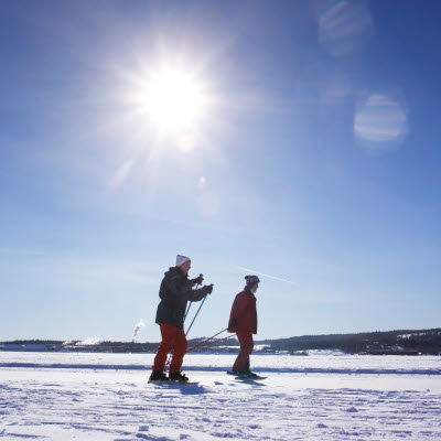 Två personer åker skidor på isen i vårsolen
