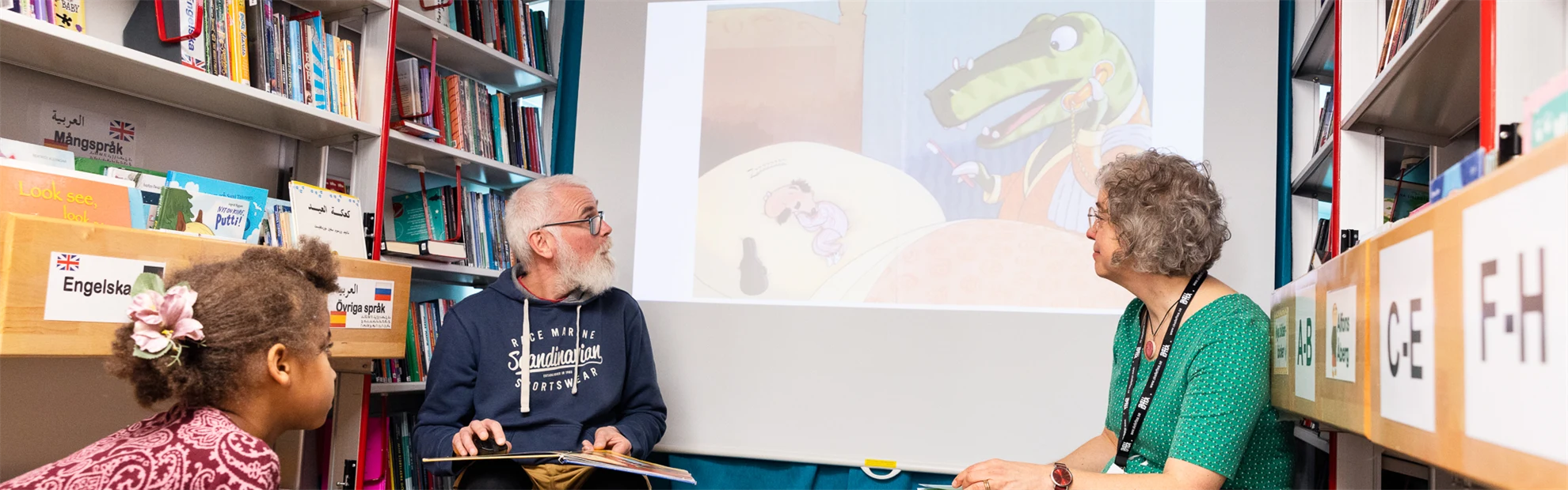 Bokbuss på barnkulturdagen på Nordanå. Två vuxna personer visar något på en bildskärm för ett barn som tittar på.