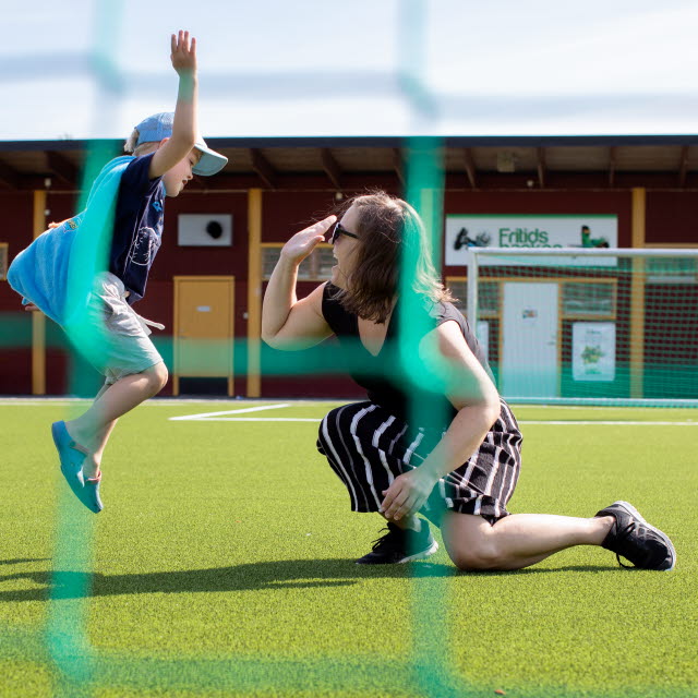 En liten pojke och en kvinna gör high five på en fotbollsplan och i förgrunden syns nätet på ett fotbollsmål.