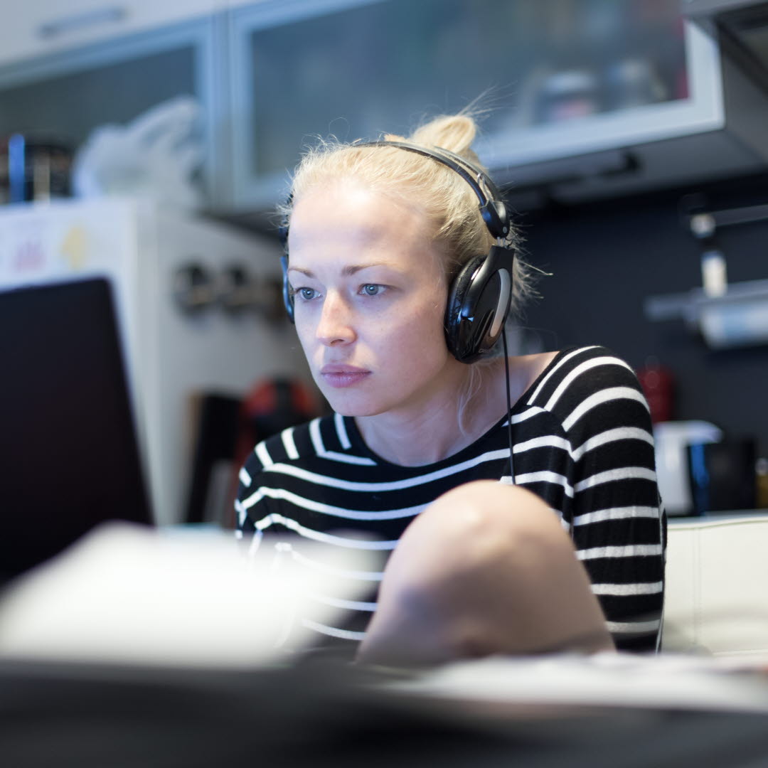 En ung kvinna sitter med lurar framför en dator och ser fokuserat på skärmen