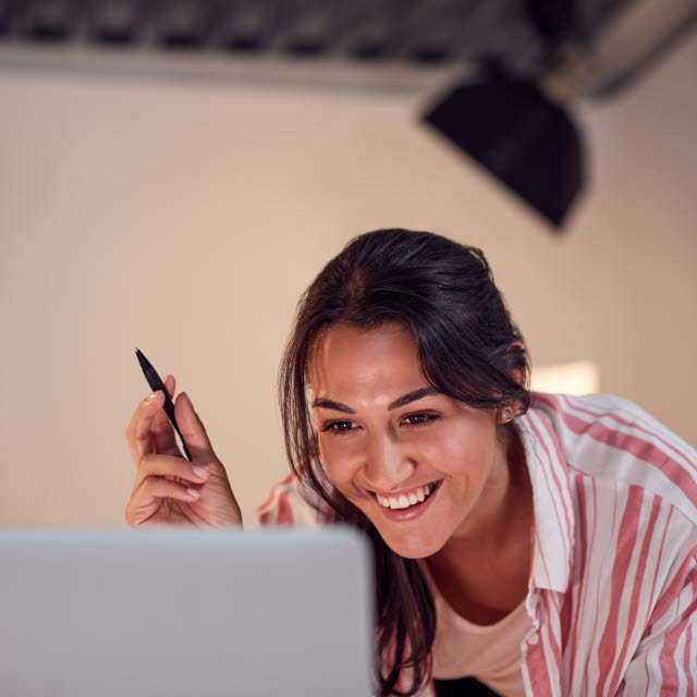 Kvinna ser in i datorskärm i en studio och ser glad ut. Hon har en digital penna i handen och vid sidan om ser man belysningsblixtar 