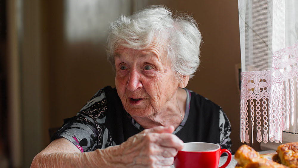 Tant sitter vid ett fönster och dricker kaffe