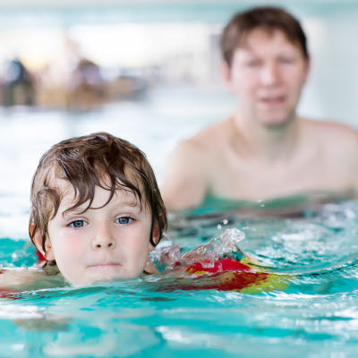 Ung man i inomhusbassäng lär pojke simma. 