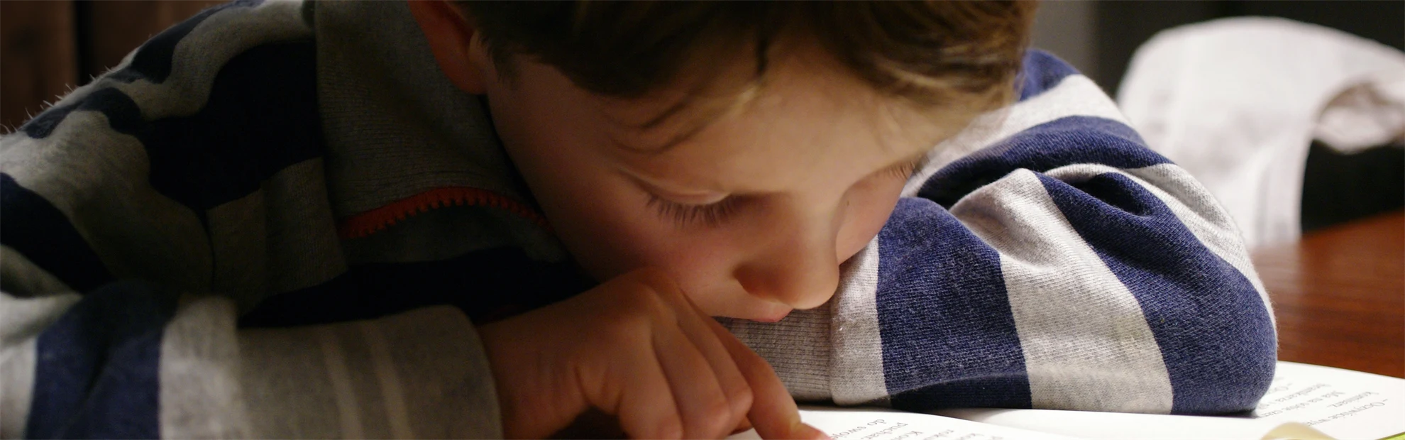 Ett barn som sitter och läser i en bok. Hen följer texten med sitt ena pekfinger och ser djupt koncentrerad ut.